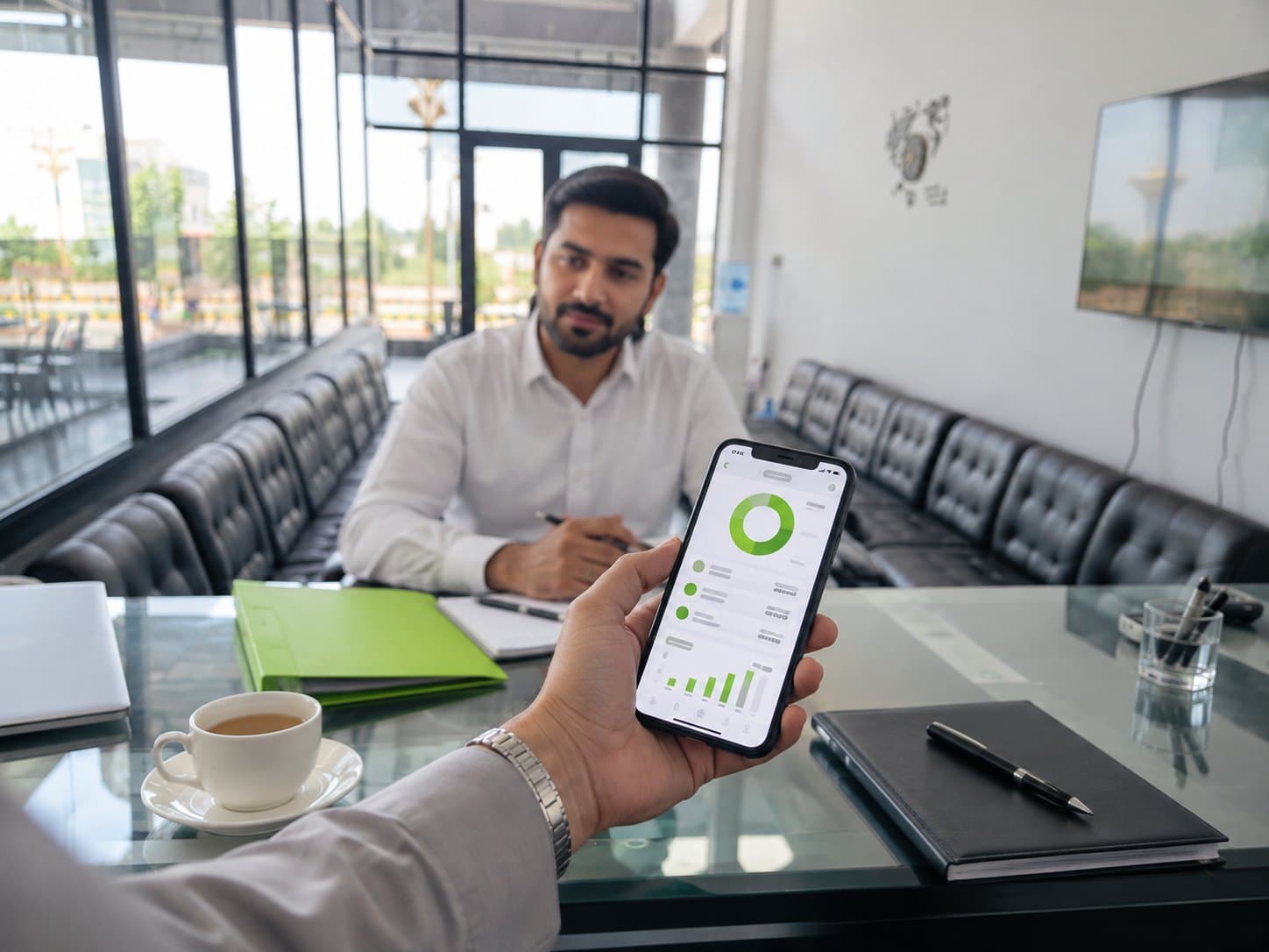 The Prime Builders investor portal on a phone, held across the office desk